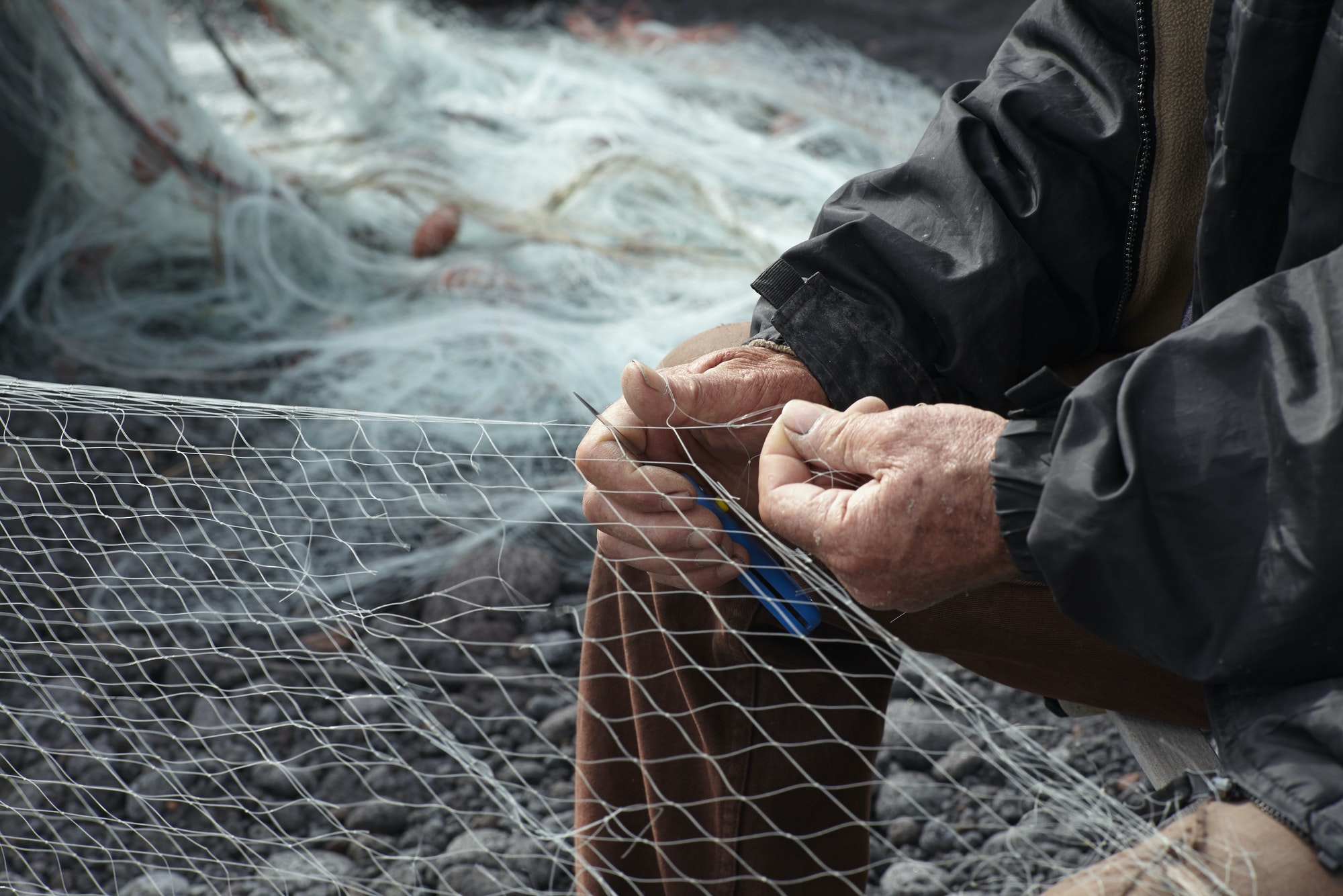 Fisherman repairing net on pebble beach
