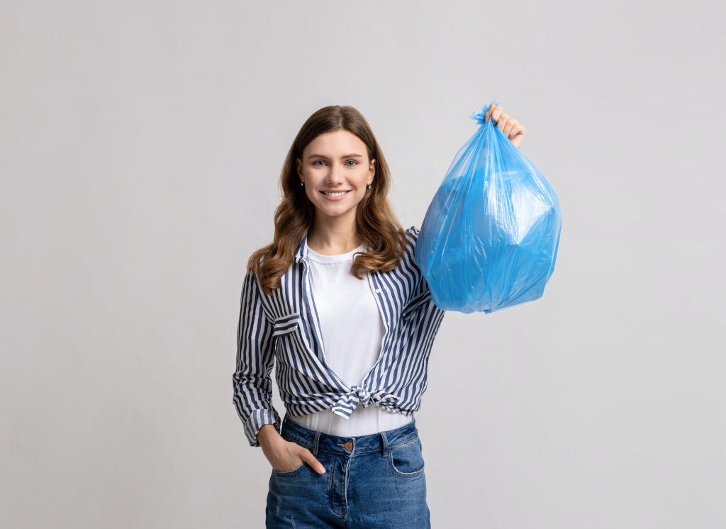 Portrait Of Smiling Millennial Lady Carrying Blue Plastic Waste Bag